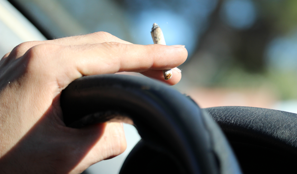 Mann konsumiert eine Cannabiszigarette beim Autofahren 