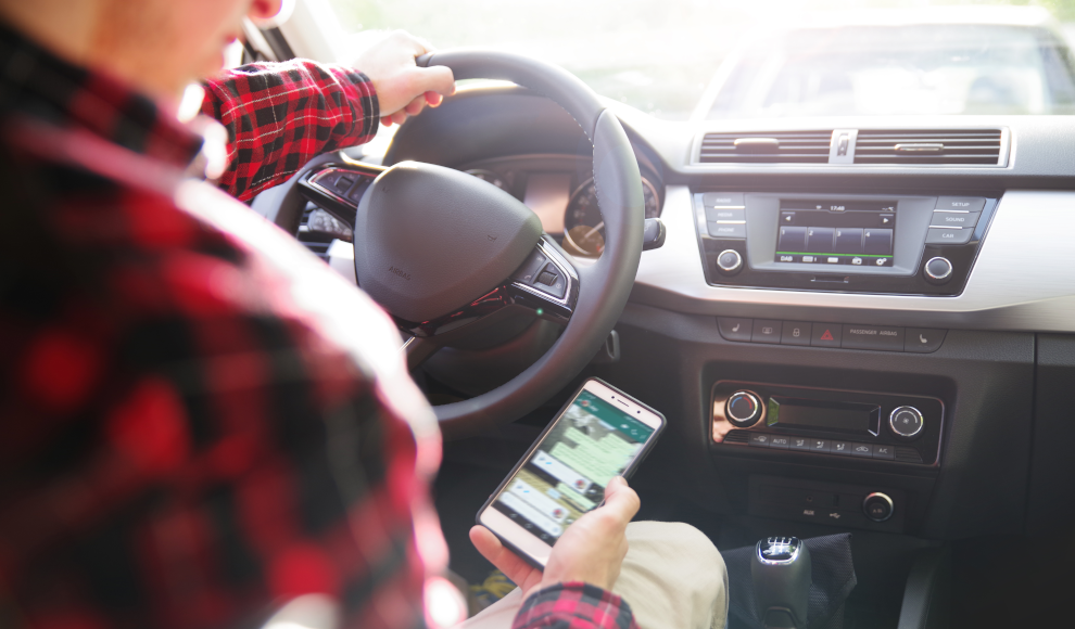 Mann schaut während der Fahrt auf sein Handy